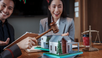 Real estate auction concept: gavel striking on model house atop laptop, with negotiators and scales...