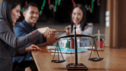 Real estate auction concept: gavel striking on model house atop laptop, with negotiators and scales of justice in background, symbolizing property law, sale, and contract agreement. © NanSan