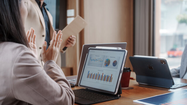 Business meeting with colleagues in modern office; tablet and laptops on table showing analytics charts and graphs during discussion.