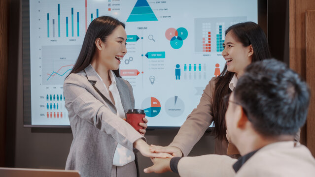 Business team stacking hands in meeting room, smiling colleagues in front of data dashboard screen, teamwork and collaboration concept.