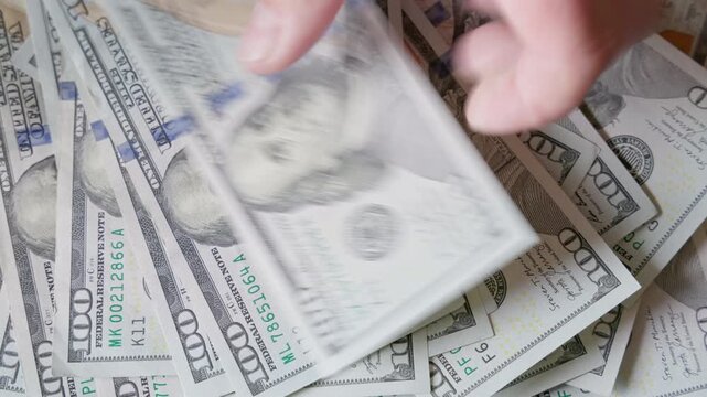 Close-up hands interacting with a pile of dollar banknotes indoors. The scene captures the texture and detail of the currency, evoking feelings of wealth and financial activity.