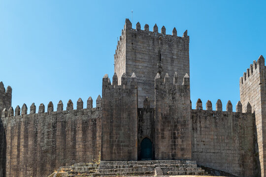 Castelo de Guimar&atilde;es, uma imponente fortaleza medieval portuguesa em pedra gran&iacute;tica com a sua torre de menagem central, ameias dentadas e arco ogival de entrada, erguida sob um c&eacute;u azul
