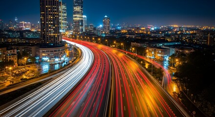 Obraz premium Endless streams of headlights sweep around a broad bend in the freeway, wrapping glowing bands of white and crimson light around clusters of high‑rise towers that watch quietly over the sprawling city