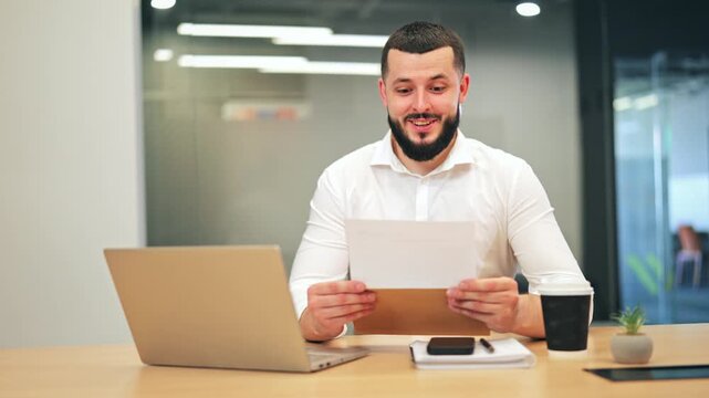 Individual at office desk opens mail, discovering surprising information. Initial shock transforms into genuine happiness, beaming with excitement after reading contents, experiences positive news.