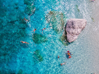 Obraz premium People enjoy a blissful day swimming and relaxing in the crystal-clear waters of Sardinia, captivated by the stunning natural beauty of Baunei. The sun shines brightly over the vibrant landscape.