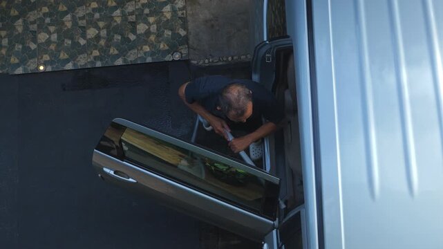 middle aged southeast asian man using vacuum cleaner to clean mpv car interior, warn morning light, natural background