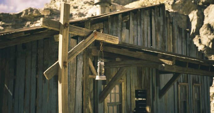 A weathered wooden building stands in an old western town, featuring a hanging lantern. Natural light casts shadows on the worn textures of the wood.