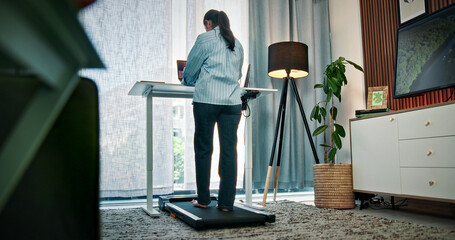 Walking, pad and back of woman for remote work, productivity and healthy habit for career. Wellness, freelance and person on treadmill with laptop for research, creative project and copywriting job © peopleimages.com