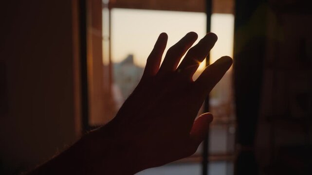 Hand silhouette against sunlight shining from outside apartment or house. Warm hot weather in early morning or sunset afternoon. Lens flare lighting dark room indoors. Waking up or energy and faith