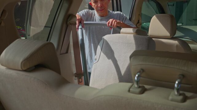 middle aged southeast asian man using vacuum cleaner to clean mpv car interior, warn morning light, natural background