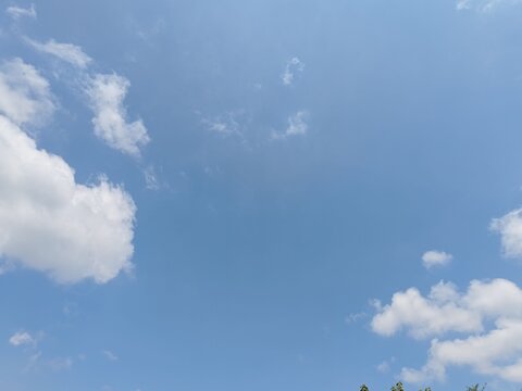 A bright, clear blue sky on a sunny day featuring soft, white clouds. This high-resolution image offers ample copy space for creative designs, travel themes, and nature-related projects.