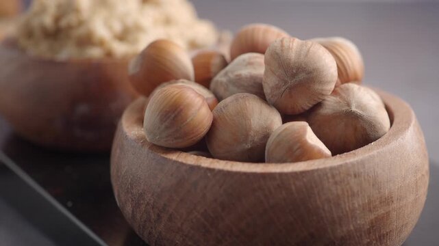 Cinematic close up of whole hazelnuts in wooden bowl on dark table surface