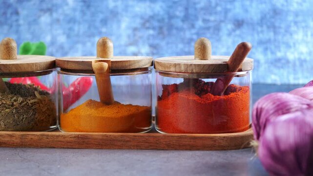 A close up view of an assortment of ground spices arranged neatly in glass jars with wooden lids on a sleek gray surface
