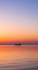 Fototapeta premium Lone cargo ship silhouetted against colorful sunset sky over calm ocean