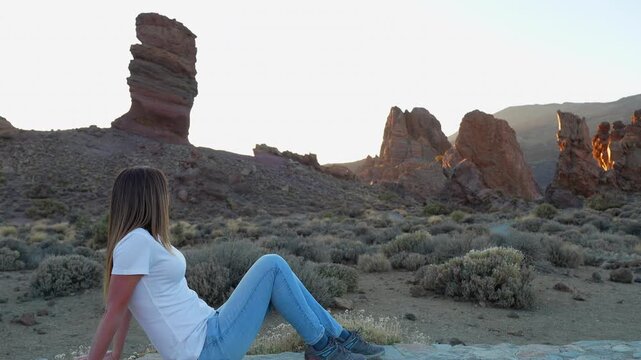 Woman sitting on a stone wall, enjoying the amazing view of the Roques de Garcia in Teide National Park, Tenerife, Spain