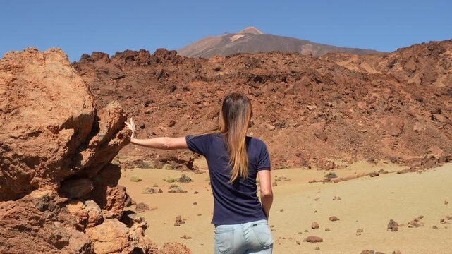 Woman looking at the volcanic scenery with the peak of Mount Teide in the background. Arid and deserted landscape on a sunny day