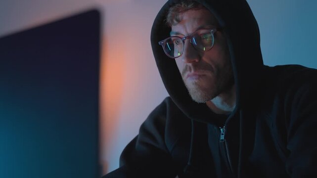 Hacker in front of a laptop putting glasses on and working. man in glasses and hoodie technology, cybersecurity, online privacy, digital communication, suspicious activity, digital communication.