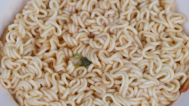 Photograph capturing textured dry noodles with vegetable flakes in bowl. Studio shot emphasizing intricate noodle swirl patterns and tiny vegetable bits for culinary presentation
