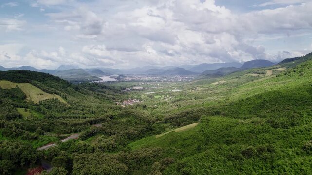 Slow hovering upward motion flying view of mountainous tropical landscape, with sunny cloudy hazy environment in the background.