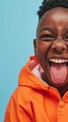 Joyful Child Smiling at Camera, Tongue Out, with Orange Jacket and Blue Background.