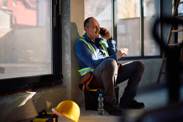 Happy construction worker talking on cell phone while having lunch break at work.