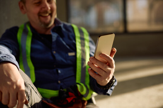 Close up of manual worker using smart phone at construction site.