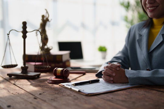 Female lawyer sitting at a wooden desk with a justice scale, gavel, and legal documents, offering professional consultation and representing the concept of law and justice