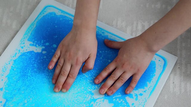 Child hands pressing colorful sensory gel mats creating moving patterns during tactile play. Sensory stimulation and occupational therapy concept for autism support and sensory integration development