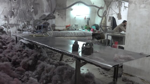 Rug weaving. Carpet establishment, small carpet mill in Iran. Stocks of sheep's wool, a worker at the machine, ready-made carpets. Behind-the-scenes video shooting