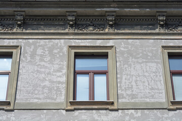 Three brown wooden windows are set into a rough weathered grey building facade featuring decorative stone consoles on the upper cornice © nahhan