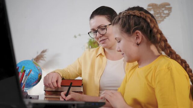 Woman tutor guiding student at laptop while pointing to screen during homeschool learning session with globe book and pencil visible hands on keyboard study and writing exercise boosting education