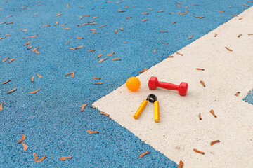 Small weights, a ball, and a pair of scissors are on a blue sports court covered with leaves