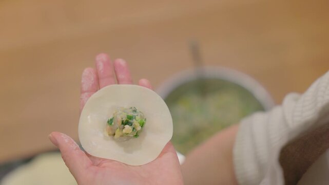 Close-up of hands wrapping gyoza filling in dumpling wrapper on wooden table