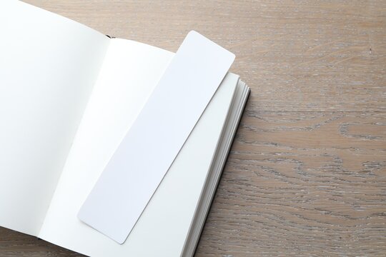 Book with white bookmark on wooden table, top view. Space for text