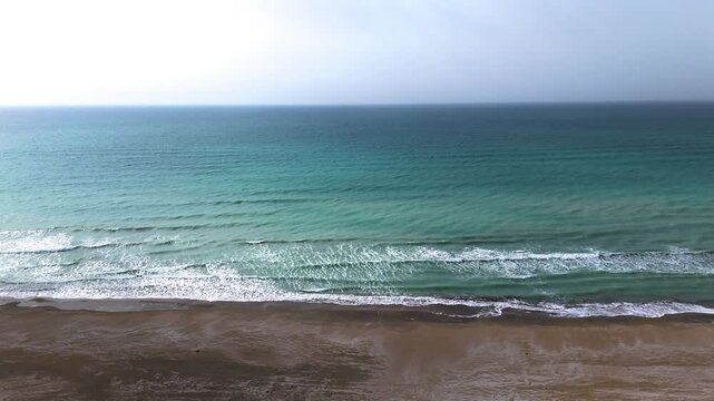 Drone footage flying from a sandy beach into the Caspian Sea waves in Aktau Mangystau Kazakhstan smooth approach over empty shoreline turquoise water and natural coastal landscape
