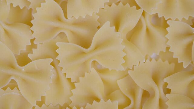 Pasta display arrangement. Golden dry bow ties showcased. Overlapping dry farfalle illuminated softly. Detailed presentation of bowed pasta pieces with gentle lighting