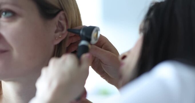 Doctor checks woman ear with otoscope during clinic examination. Medical specialist aims light inspecting canal carefully while patient sits still