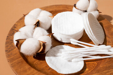 Cotton pads and cotton swabs, delicate cotton flowers on wooden plate, close-up. Concept of eco-friendly makeup removers, facial skin care. Beauty, health, and personal hygiene © olgaarkhipenko
