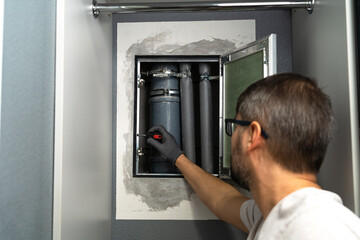 Plumber installs hidden technical inspection hatch in wall to access sewer pipes in kitchen or bathroom. Sewerage