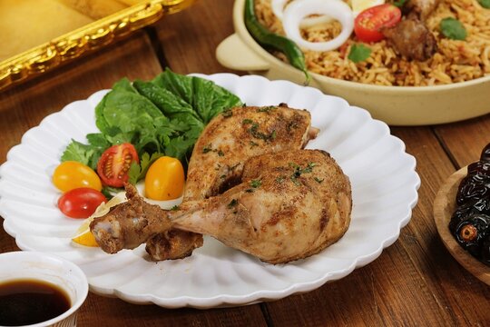 Traditional Middle Eastern dajaj mashwi grilled chicken served with fresh salad, cherry tomatoes, and spiced rice on wooden table. Authentic Arabic cuisine food photography.