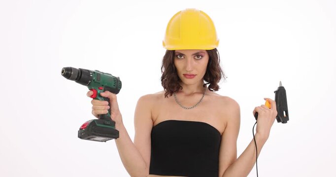 Construction worker imitates gunshot gesture by holding power drill in hands on white background. Female in hard hat simulates gunshot. Slow motion