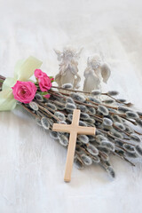Fototapeta premium Easter and Palm Sunday holiday background. Bouquet of pussy willow and roses, wooden cross, angel figurines on light table close up. symbol of Easter, prayer, faith, orthodox Church, religion concept