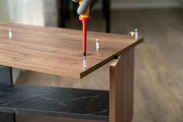 Male hands assemble nightstand using screwdriver. Tightening connecting bolt. Process of assembling furniture. Furniture assembler installs fasteners