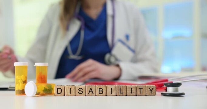 Miniature wooden blocks form word Disability on desk with medicine. Woman doctor carefully studies documents containing medical history of patient