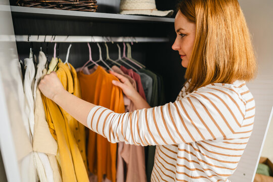 Woman organizing closet with various clothes representing overconsumption