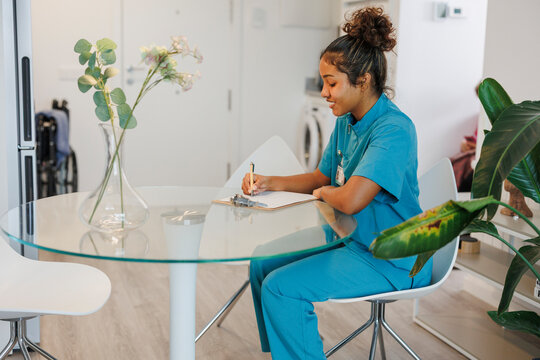 Nurse writing on clipboard at household table for medical checkup