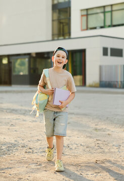 Smiling kid walking outdoors with book and backpack on sunny day