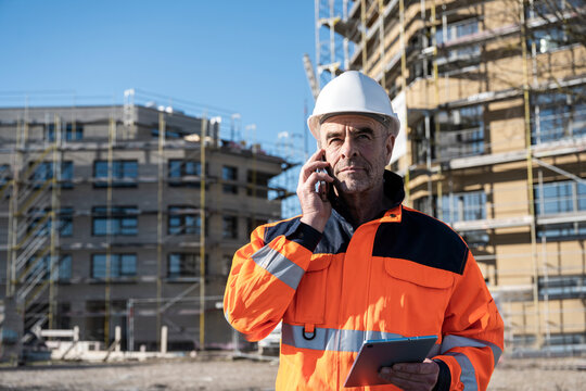 Engineer in high visibility jacket at construction site with tablet and phone