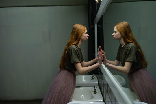 Red haired freckled woman with tulle skirt gazing at reflection in mirror