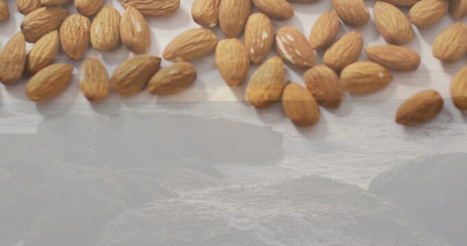 Almonds sliding in from top, spreading across light tray and covering seascape to show abundance